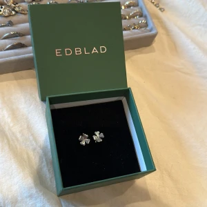 Silverörhängen från Edblad - Säljer ett par eleganta silverörhängen från Edblad. De har en stilren design med en fyrklöverform som ger en touch av lyx. Perfekta för att komplettera din look med en subtil glans.