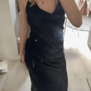 Svart långklänning med v-ringning - Elegant svart långklänning med v-ringad design och smala axelband. Perfekt för en stilren look. En liten skada vid ena bandet på framsidan då de lossnade så sydde tillbaka de, men är absolut inget man tänker på. Är bara använd en gång