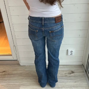 Blå jeans från Lee - Säljer ett par klassiska blå jeans från Lee. De har en bootcut-stil och är lågmidjade med en snygg passform. Perfekta för en avslappnad look. Midjemått 36x2 innerbens längd 77cm 