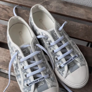 Grå sneakers från Christian Dior - Snygga grå sneakers från Christian Dior med ett ikoniskt mönster och vit sula. Skorna har snörning och märkesdetaljer på sidan och tungan. Perfekta för en stilren look. I jätte bra skick och storlek 38. Köpte från Vestiaire Collective för 9300kr och säljer för 3850kr har ingen box. Går att diskutera pris 