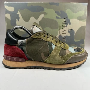 Valentino Rockrunner i camouflage - Snygga Valentino Rockrunner sneakers i ett coolt camouflagemönster. Skorna har en mix av gröna, bruna och röda nyanser med detaljer i mocka och skinn. Perfekta för att ge din outfit en edgy touch. Endast box medföljer. Ny pris 6499