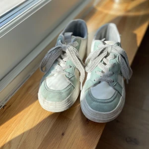 Grönvita sneakers med snörning - Snygga sneakers i en fräsch kombination av grönt och vitt. Skorna har en klassisk design med snörning och rund tå. Fin snörnings fläta på sidan. Snörena är vita och flätade. Perfekta för en avslappnad sommar stil.