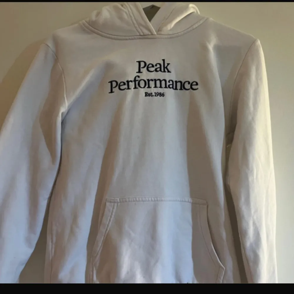 Säljer en stilren vit hoodie från Peak Performance med svart text på bröstet. Den har en klassisk känguruficka och en bekväm huva. Skulle säga storlek xs. Lappen är bort klippt. . Neuletakit & Villapaidat.