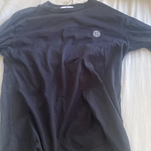 Svart långärmad tröja från Stone Island - Säljer en stilren svart t-shirt från Stone Island med rund hals och korta ärmar. Den har en liten logga på bröstet. Perfekt för en casual look.