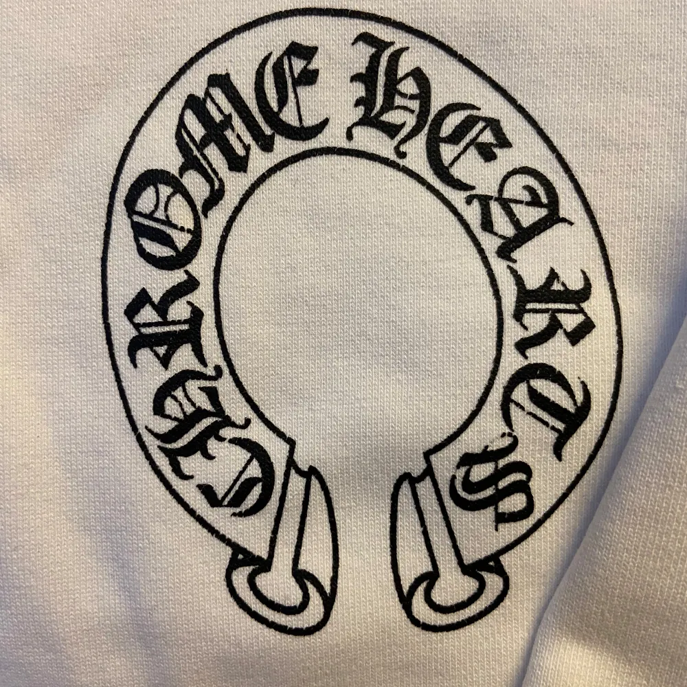 Säljer en vit hoodie från Chrome Hearts med dragkedja och detaljerade svarta tryck på ärmarna och ryggen. Hoodien har en justerbar huva och är perfekt för en stilren look. Den har också ett unikt märke på dragkedjan.. Neuletakit & Villapaidat.