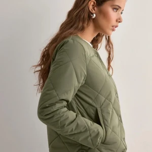 Olivgrön quiltad jacka - Snygg olivgrön quiltad jacka med knappar framtill. Jackan har en normal passform och bra armar, perfekt för höst och vår. Den quiltade designen ger en stilren look. Ordinare pris 699kr och använd 1 gång