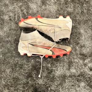 Puma ultra PRO - Snygga fotbollsskor i beige och orange med snörning och rund tå. Skorna har en modern design med svarta detaljer och är perfekta för fotbollsplanen.