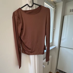 Brun långärmad topp - Säljer en stilren brun långärmad topp med rund halsringning. Perfekt för en avslappnad look eller att klä upp med accessoarer. Passar bra till både jeans och kjol.