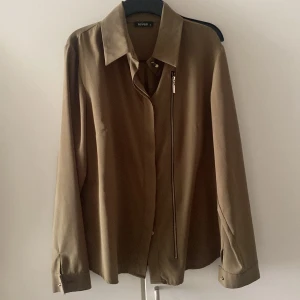 Olivgrön skjorta från Fever - Snygg olivgrön skjorta från Fever med en unik dragkedjedetalj framtill. Skjortan har långa ärmar och en klassisk krage. Perfekt för en stilren look. M/S