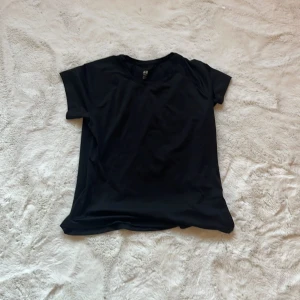 Svart sport t-shirt från H&M - Säljer en svart sport t-shirt från H&M. Den är kortärmad och tillverkad i ett lätt och andningsbart syntetmaterial, perfekt för träning. T-shirten har en diskret design med en liten reflekterande detalj på baksidan.