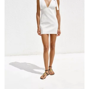 Vit kortklänning med rosett - Elegant vit kortklänning med djup v-ringning och dekorativa rosetter på axlarna. Perfekt för sommarens festligheter. Storlek s som är slutsålt på hemsidan 