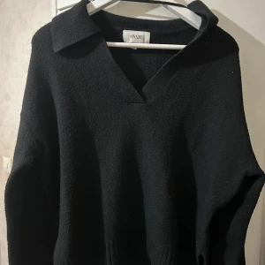 Svart stickad tröja från Aware - Säljer en stilren svart stickad tröja från Aware. Tröjan har en v-ringad design med en bred krage och långa ärmar. Perfekt för kyligare dagar.