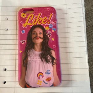 Rosa mobilskal med Soy Luna-motiv - Säljer ett färgglatt rosa mobilskal med ett motiv från Soy Luna. Skalet har texten 'Like!' och olika dekorationer som stjärnor och hjärtan. Perfekt för fans av serien som vill ge sin telefon en personlig touch.