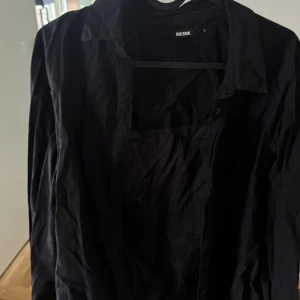 Svart skjorta från Bik Bok - Snygg svart skjorta från Bik Bok i storlek S. Skjortan har en klassisk krage och knappar framtill. Perfekt för en stilren look.