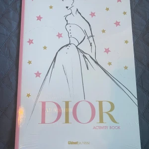 Dior Activity Book - Upptäck Dior Activity Book, en elegant och kreativ bok som bjuder in dig till haute couture-världen. Med skisser, foton och tyger kan du drömma, färglägga och skapa. Perfekt för modeentusiaster som vill utforska Dior-stilen.