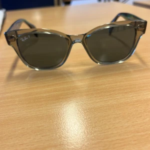 Solglasögon från Ray-Ban - Snygga solglasögon från Ray-Ban med en transparent brun båge och mörka linser. Perfekt för soliga dagar. Kommer med ett stilrent svart fodral för säker förvaring. Kvitto fina ny pris 2700kr
