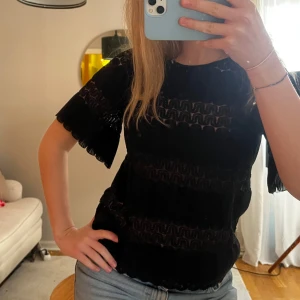 Svart blus med genomskinliga detaljer - Snygg svart blus med korta ärmar och vackra spetsdetaljer. Perfekt för att klä upp en vardagsoutfit eller för fest! 