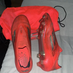  fotbollsskor  - Säljer ett par röda fotbollsskor från Adidas med svarta detaljer och dobbar för gräsplan. Jätte sköna men använd ett tag nu men inga konstigheter vid strumpan som har gått upp lite