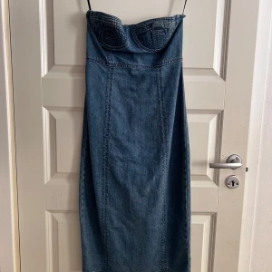 Jeansklänning från Forever 21 - Snygg axelbandslös jeansklänning från Forever 21. Klänningen har en tight passform med en slits baktill och dragkedja för enkel påklädning. Perfekt för en trendig look!