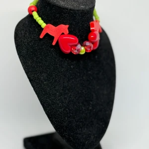 Färgglatt armband  med hjärtan och dalahästar - Unikt armband  med röda hjärtan och dalahästar, kompletterat med gröna och röda pärlor. Perfekt för att ge en färgglad touch till din outfit.