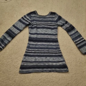 Blå och ljusblå randig stickad kortklänning - Säljer en mysig blå och ljusblå randig stickad klänning med långa ärmar. Perfekt för kyliga dagar med sin mjuka och bekväma passform. Men ävrn perfekt för stranden som en coverup Tröjan har en u-ringning i ryggen. 