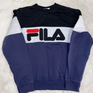 Tröja från FILA i blått och svart - Snygg tröja från FILA i blått och svart med vit och röd detalj. Tröjan har långa ärmar och en klassisk passform. Perfekt för en avslappnad stil.