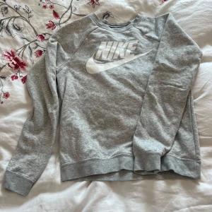 Grå sweatshirt från Nike - Säljer en klassisk grå sweatshirt från Nike med deras ikoniska logga i vitt på bröstet. Tröjan har långa ärmar och en rund halsringning. Perfekt för en avslappnad stil.