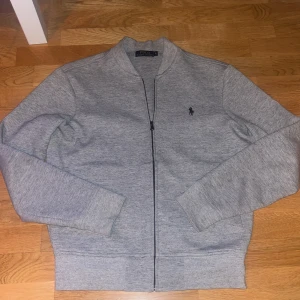 Grå tröja från Polo Ralph Lauren - Säljer en stilren grå tröja från Polo Ralph Lauren. Tröjan har en dragkedja framtill och en liten broderad logotyp på bröstet. Perfekt för en avslappnad och snygg look. Nypris runt 1500 kr. Pris kan diskuteras vid snabb affär🤙