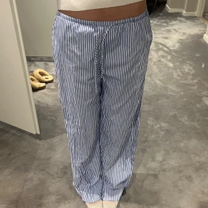 Randiga pyjamasbyxor i blått och vitt - Säljer ett par bekväma pyjamasbyxor med blå och vita ränder. Byxorna har en elastisk midja med snörning för justerbar passform. Aldrig använt.