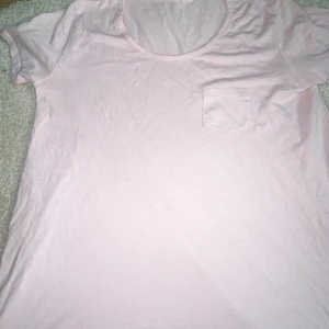 Ljusrosa t-shirt från Brandy Melville  - Säljer en ljusrosa t-shirt med en liten bröstficka. Perfekt för en avslappnad stil. T-shirten har korta ärmar och en rund halsringning. Från brandy Melville i USA!🇺🇸❤️