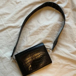 Svart axelväska  - Svart axelväska med orm/krokodilmönster.