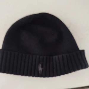 Svart mössa raulph lauren - Snygg svart mössa med ribbad kant och en diskret broderad logga framtill. Perfekt för kyliga dagar och en stilren look.