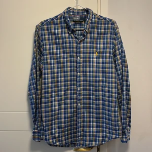 Rutig skjorta från Polo Ralph Lauren - Säljer en snygg rutig skjorta från Polo Ralph Lauren i blått, gult och vitt. Skjortan har en slim fit passform och långa ärmar. Perfekt för en stilren look!