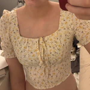 Blommig topp - En blommig söt kort topp med puffade ärmar och  en fyrkantig u-ringning. Toppen har resår på baksidan så det blir enkelt att ta på sig den.