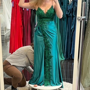 Grön balklänning med spetsdetaljer - Pris går att diskutera! Elegant grön långklänning med smala axelband och v-ringad spetsöverdel. Klänningen har en vacker spetsapplikation längs framsidan och en snörning i ryggen för en perfekt passform. Perfekt för en speciell kväll. Klänningen är samma färg som spetsdelen, ser ljusare ut på bild än i verkligheten! Original pris 4000 +uppsyning