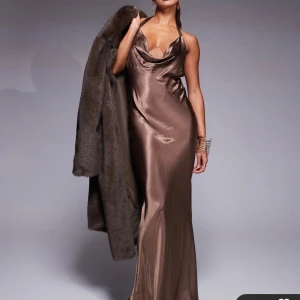 Brun satinklänning, balklänning - Jättefin brun långklänning med en halterneck-design. Klänningen har en vacker drapering och en öppen rygg. Perfekt som balklänning!! Endast provad, passade ej i storlek.