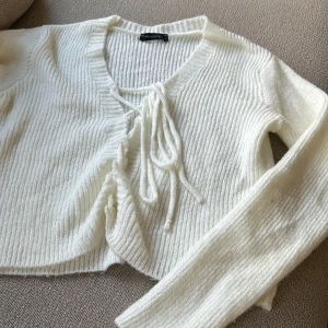 Vit ribbad kofta  - Säljer en vit ribbad kofta med knytning framtill. Den har långa ärmar och är perfekt för lager-på-lager under kyligare dagar. Enkel och stilren design som passar till det mesta.