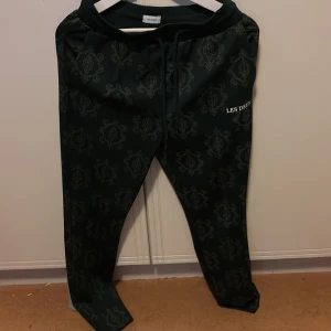 Mönstrade byxor från Les Deux - Snygga mörkgröna byxor från Les Deux med ett unikt mönster. Byxorna har snörning i midjan och en avslappnad passform. Perfekta för en stilren look.