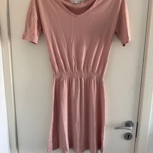 Rosa klänning från 157 - Säljer en söt rosa klänning från 157 i storlek XS. Klänningen har korta ärmar och en v-ringad hals. Den är elastisk i midjan för en bekväm passform. (Katt o kanin finns i hemmet) 