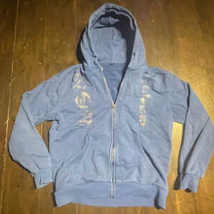 Blå RhineStone hoodie - Säljer en blå RhineStone hoodie. Den har en mysig huva och praktiska fickor framtill. Perfekt för att lägga till lite bling i vardagen!