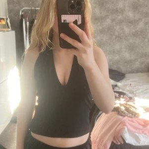 Svart halterneck topp - Snygg svart halterneck topp med djup urringning och öppen rygg. Perfekt för en kväll ute eller en somrig dag. Enkel och stilren design som passar till det mesta.