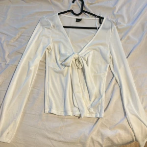Vit omlottopp med knyt från Gina Tricot - Supersnygg vit omlottopp från Gina Tricot. Aldrig använd men prislappen är av då jag endast testat den. Säljer pga den kom aldrig till användning och måste rensa.