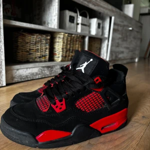 Nike Air Jordan 4 svart/röd sneakers ”Red thunder” - Säljer ett par Nike Air Jordan 4 sneakers i svart och rött med klassisk Jumpman-logga på tungan och hälen. Skorna har meshpaneler, snörning och detaljer i syntet och mocka. Sulan är platt med röda inslag och skorna har en sportig, chunky siluett som sticker ut. Se på sista bilden, originalpris 5999kr.