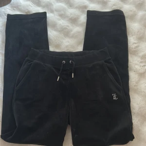 Svarta Juicy Couture mjukisbyxor S - Svarta mjukisbyxor från Juicy Couture i storlek S, med glittrande strassdetaljer på fickan och stor 'Juicy'-text på baken. Byxorna har snörning i midjan och är gjorda i mjuk sammet för en lyxig och chill vibe.