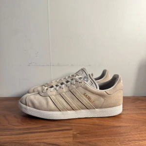 Beige Adidas Gazelle sneakers  - Säljer ett par stilrena beige Adidas Gazelle sneakers i mocka i bra skick. Perfekta nu till sommaren/hösten