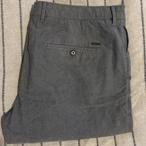 Hugo Boss chinos - Hugo Boss chinos – grå, strl 34 Grå chinos från Hugo Boss med diskret rutigt mönster. Klassisk passform och stilren look. I mycket bra skick!