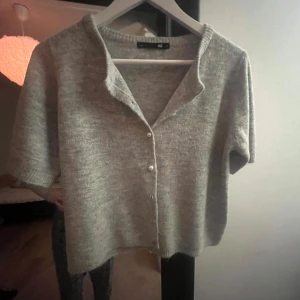Grå stickad kofta  - Mysig grå stickad kofta från 157 i storlek M. Koftan har korta ärmar,den har pärlknappar framtill. Perfekt för lager-på-lager och chill stil. Materialet är mjukt och ger en skön känsla. Enkel att matcha med jeans eller kjol.