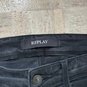 Svarta Replay jeans slim fit - Svarta jeans från Replay med klassisk femficksdesign och snygga detaljer på bakfickorna. Slim fit-modell med smalare ben och midja, perfekta för en clean och modern look. Materialet är mjukt och stretchigt jeans.