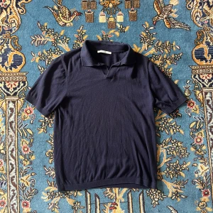 Marinblå pikétröja från A Day's March - Snygg marinblå pikétröja från A Day's March i storlek M. Tröjan har klassisk krage och korta ärmar, perfekt för en chill och stilren look. Materialet känns mjukt och är stickat, vilket ger en skön känsla mot huden. Passar dig som gillar enkel och clean stil.