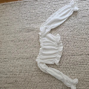 Vit offshoulder blus med volanger - Superfin vit blus med offshoulder-design och långa puffiga ärmar. Blusen har volangdetaljer vid hals och midja samt elastiska partier som ger en snygg passform. Perfekt för dig som gillar romantisk och trendig stil.